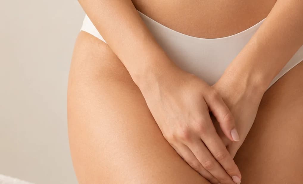 A woman's hands resting over her pelvis, in cream underwear